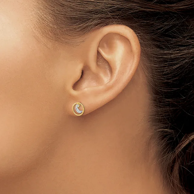 A person wearing a small silver crescent moon stud earring with a blue stone in the center, shown on their earlobe from a side profile view.