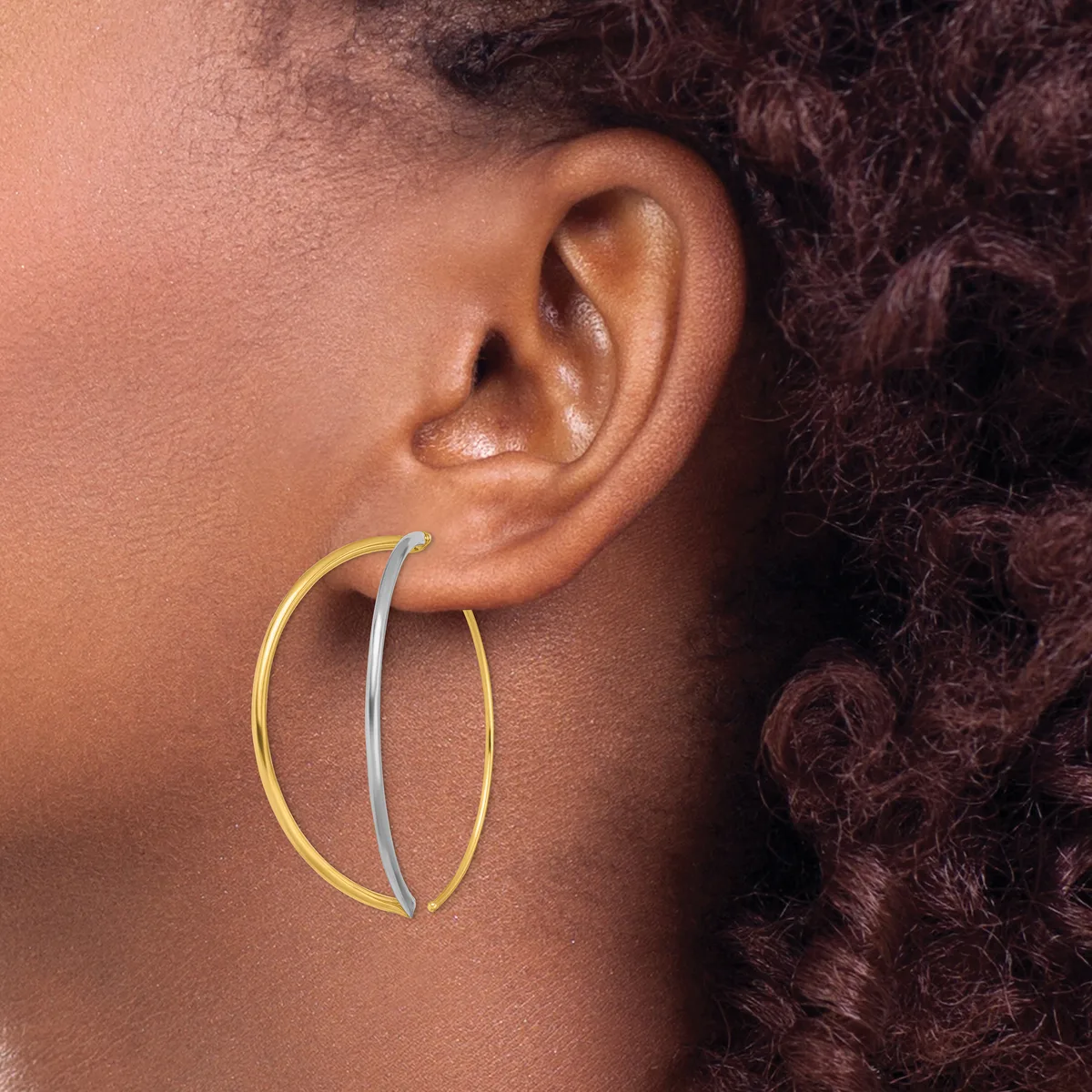 A person wearing two-tone hoop earrings with a gold outer curve and silver inner curve, shown in profile against their ear.