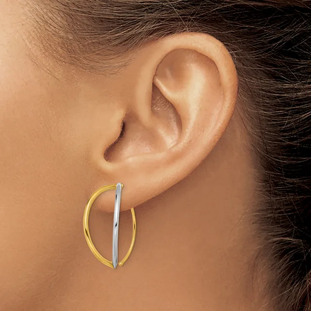 A close-up view of a person's ear wearing two-tone hoop earrings with a gold outer band and silver inner bar detail.