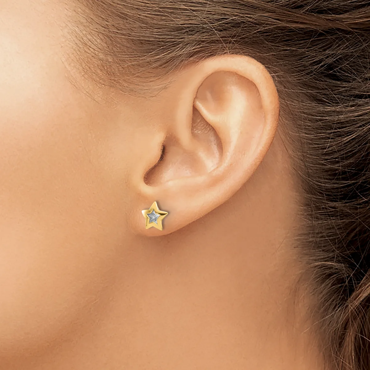 A small gold star-shaped stud earring is worn on the earlobe of a person with brown hair.