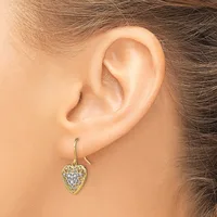 A person wearing a gold heart-shaped dangle earring with a filigree pattern and small gemstones, shown from the side view of their ear.