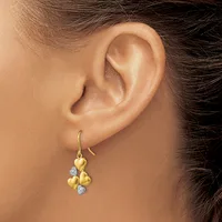 A person wearing gold drop earrings with heart-shaped charms and diamond accents, shown from the side view of their ear and neck.