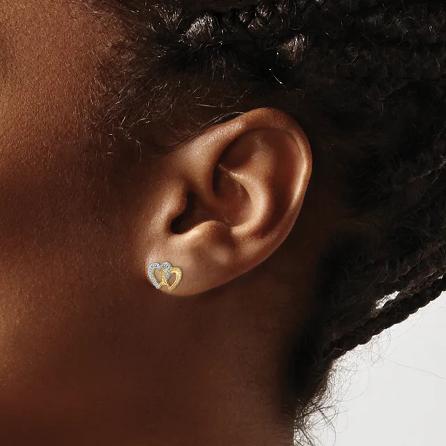 A person wearing a small gold heart-shaped earring with diamond accents in their pierced earlobe, shown in profile view.
