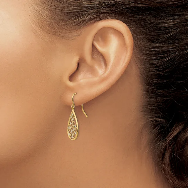 A person wearing a pair of gold teardrop earrings with filigree detailing, shown from the side profile of their ear and neck.