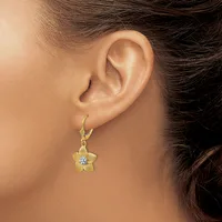 A person wearing a yellow flower-shaped earring with a central diamond or crystal stone, suspended from a gold hook earring.