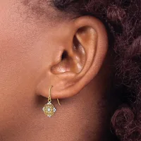 A close-up view of a person's ear wearing a gold-toned filigree drop earring with a quatrefoil design and hook fastening.