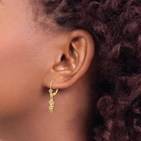 A person wearing a gold hoop earring with a dangling decorative charm, shown from the side profile against their ear and dark curly hair.