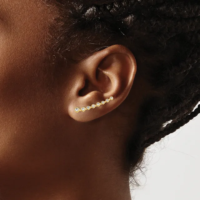 A person wearing a curved ear climber earring with small round crystals set in gold-tone metal along the upper ear.