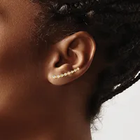 A person wearing a curved ear climber earring with small round crystals set in gold-tone metal along the upper ear.
