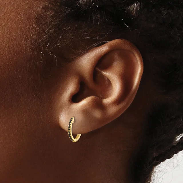 A gold textured hoop earring worn in the earlobe of a person with brown skin and dark hair.
