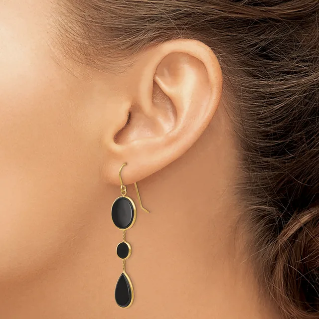 A person wearing a silver drop earring with three graduated black oval stones suspended on a hook, shown from the side view of their ear.