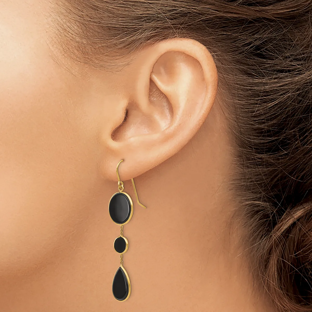 A person wearing a silver drop earring with three graduated black oval stones suspended on a hook, shown from the side view of their ear.