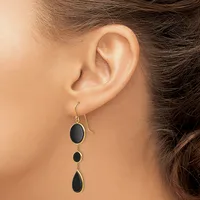 A person wearing a silver drop earring with three graduated black oval stones suspended on a hook, shown from the side view of their ear.