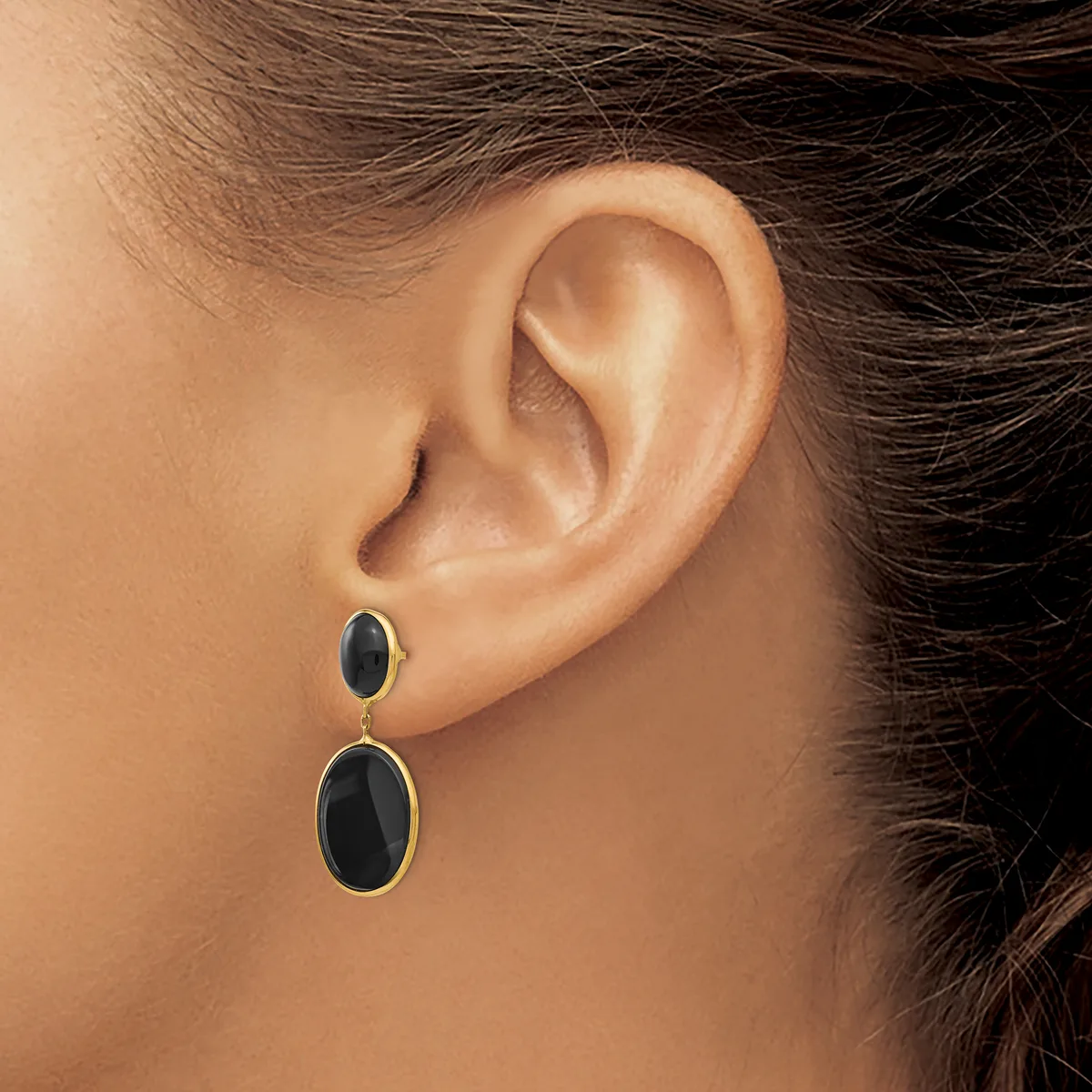 A person wearing black oval drop earrings with gold bezels and posts, shown from the side view of their ear and neck.