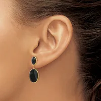 A person wearing black oval drop earrings with gold bezels and posts, shown from the side view of their ear and neck.