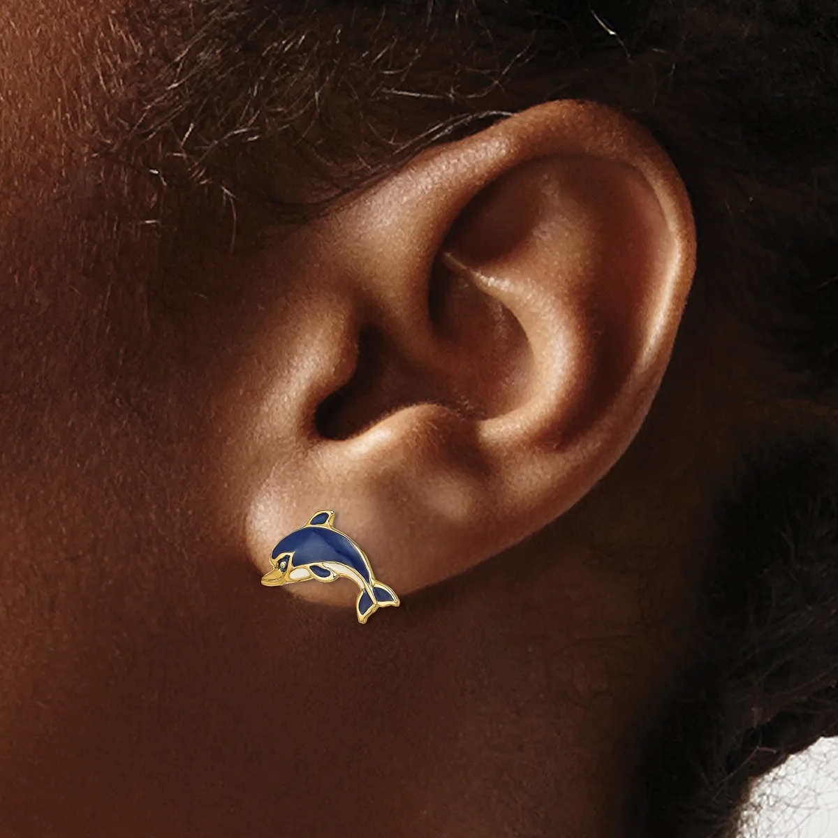 A dolphin-shaped earring in blue enamel with gold trim on a person's earlobe.