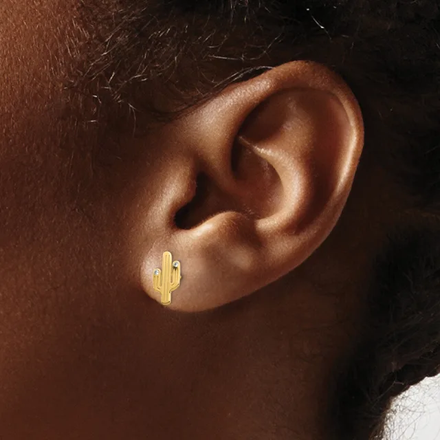 A small gold cactus-shaped stud earring worn in the earlobe of a person with brown skin.