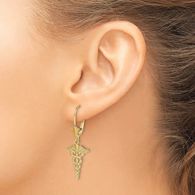 A person wearing a gold caduceus pendant earring on a hook-style earwire, shown from the side view of their ear.