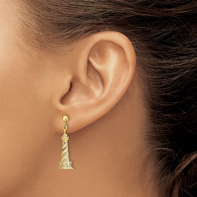 A person wearing a gold lighthouse-shaped dangle earring with a textured spiral pattern on the tower, shown from the side view of their ear.