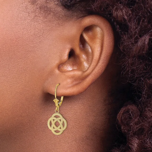 A gold-toned drop earring with an interlocking Celtic knot design hangs from a curved hook on a person's earlobe.