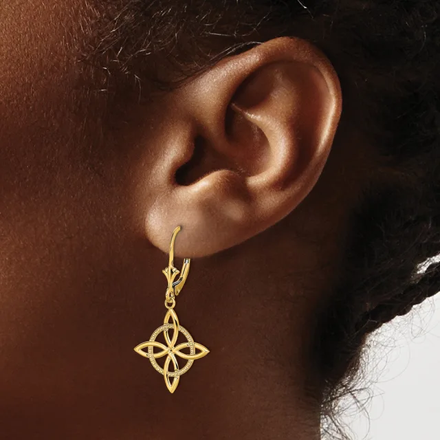 A gold four-pointed star earring with interlocking loops hangs from a lever-back hook on a person's earlobe.
