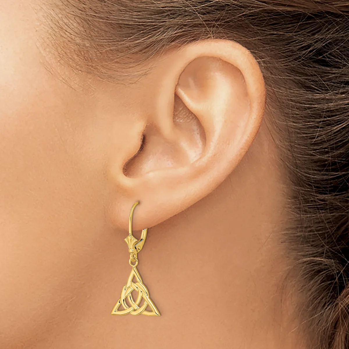 A gold-toned triangular pendant earring with interlocking Celtic knot design hangs from a lever-back hook on a model's earlobe.