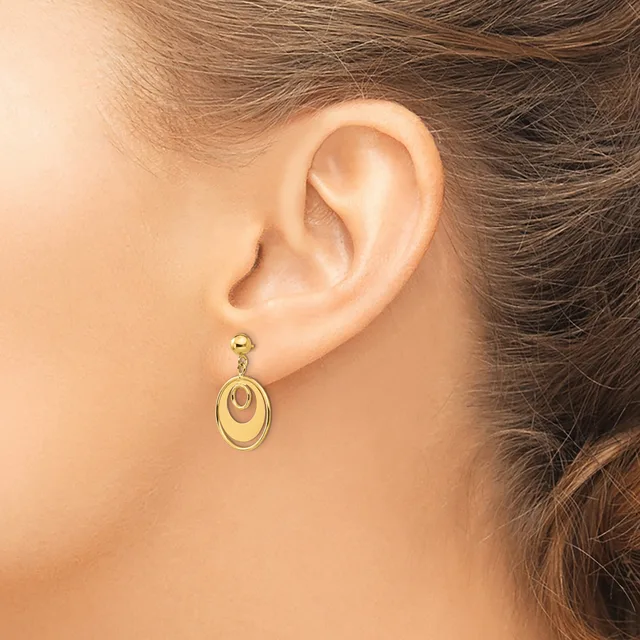 A woman wearing gold-toned oval dangle earrings with nested concentric rings, shown from the side profile view of her ear.
