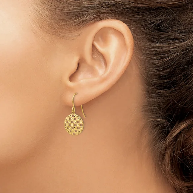 A woman wearing a gold-toned drop earring with a textured circular disc pendant on a curved hook, shown from the side view of her ear and neck.