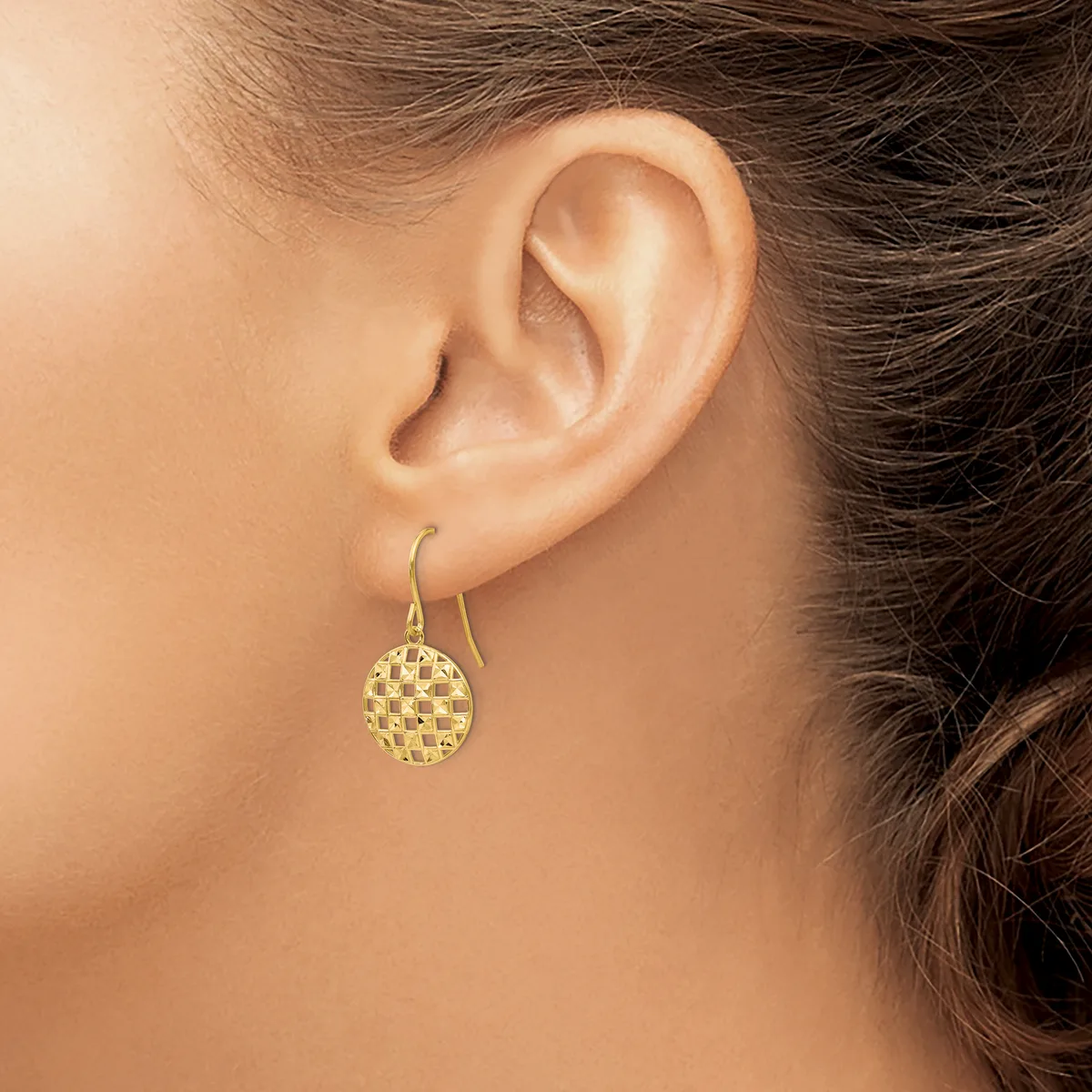 A woman wearing a gold-toned drop earring with a textured circular disc pendant on a curved hook, shown from the side view of her ear and neck.
