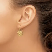 A woman wearing a gold-toned drop earring with a textured circular disc pendant on a curved hook, shown from the side view of her ear and neck.