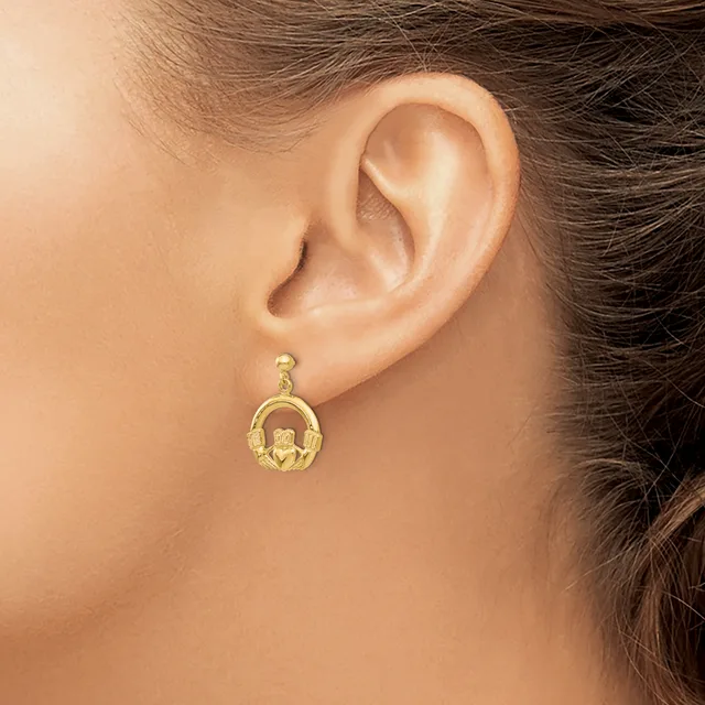 A gold drop earring with a horseshoe and claddagh design hangs from a woman's earlobe.