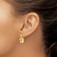 A person wearing a small gold flower-shaped drop earring on a hook post, shown from the side view of their ear and neck.