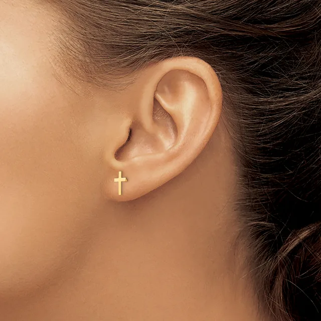 A close-up view of a person's ear wearing a small gold cross stud earring in the lobe.