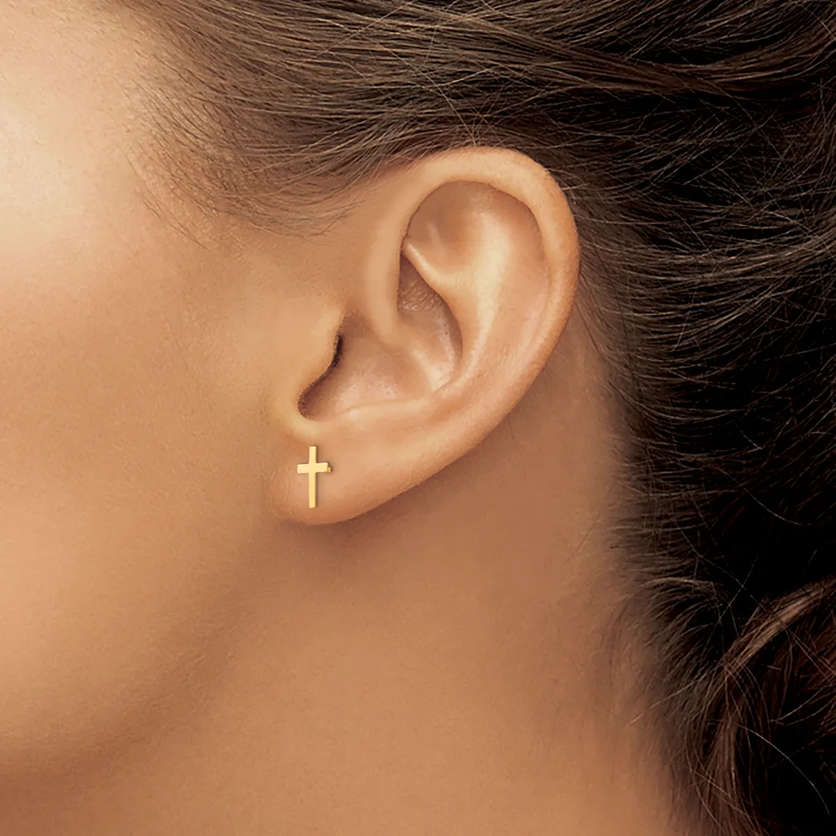 A close-up view of a person's ear wearing a small gold cross stud earring in the lobe.