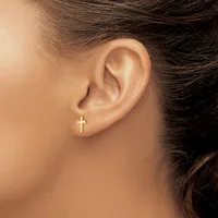 A close-up view of a person's ear wearing a small gold cross stud earring in the lobe.