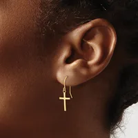 Close-up of a person's ear wearing a gold cross pendant hanging from a thin curved hook earring.