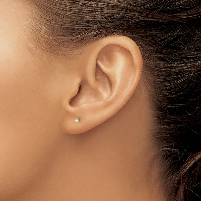 A small diamond stud earring in a pierced earlobe, shown from the side profile of a person with dark hair.