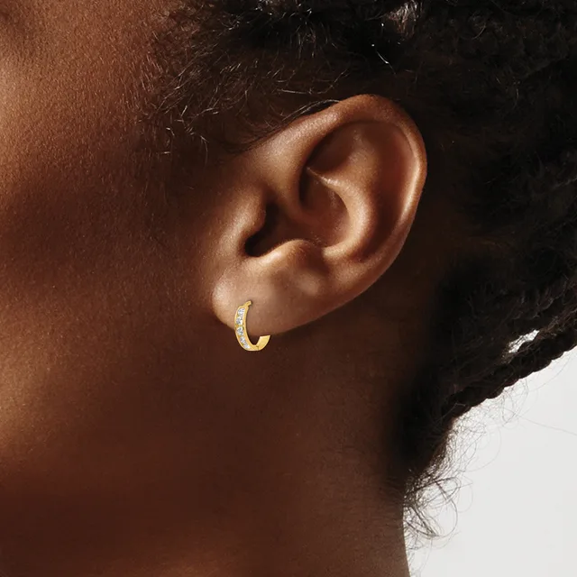A close-up side view of a person's ear wearing a small gold hoop earring with a textured surface.