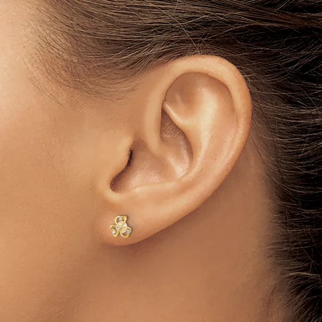 A person wearing a small gold stud earring with a clover or trefoil design set with small stones in the earlobe.