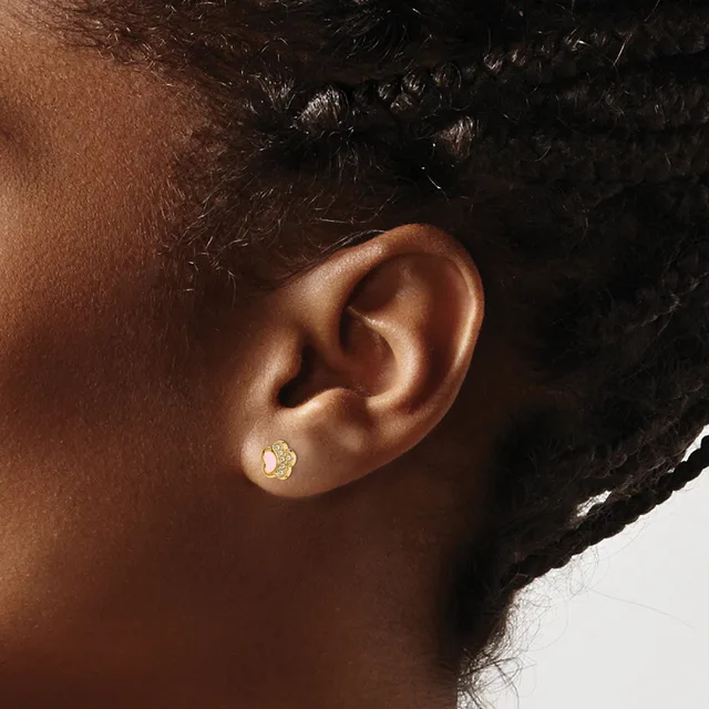 A person wearing a small gold stud earring with a textured finish in their earlobe, shown in profile against a white background.