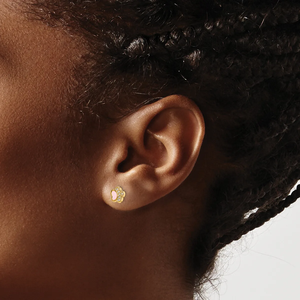 A person wearing a small gold stud earring with a textured finish in their earlobe, shown in profile against a white background.