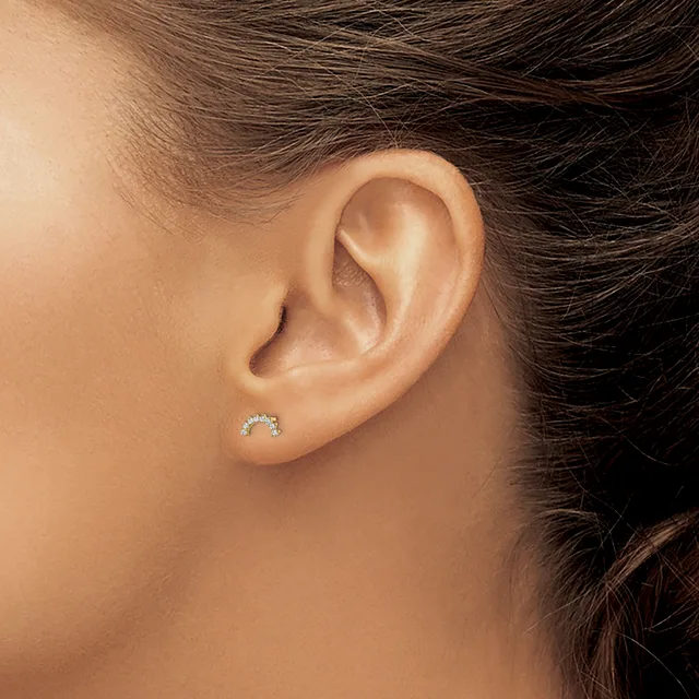 A close-up view of a person's ear wearing a small curved stud earring with sparkling stones set in metal.