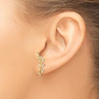 A gold leaf-shaped earring with small diamond accents is worn on a person's earlobe.