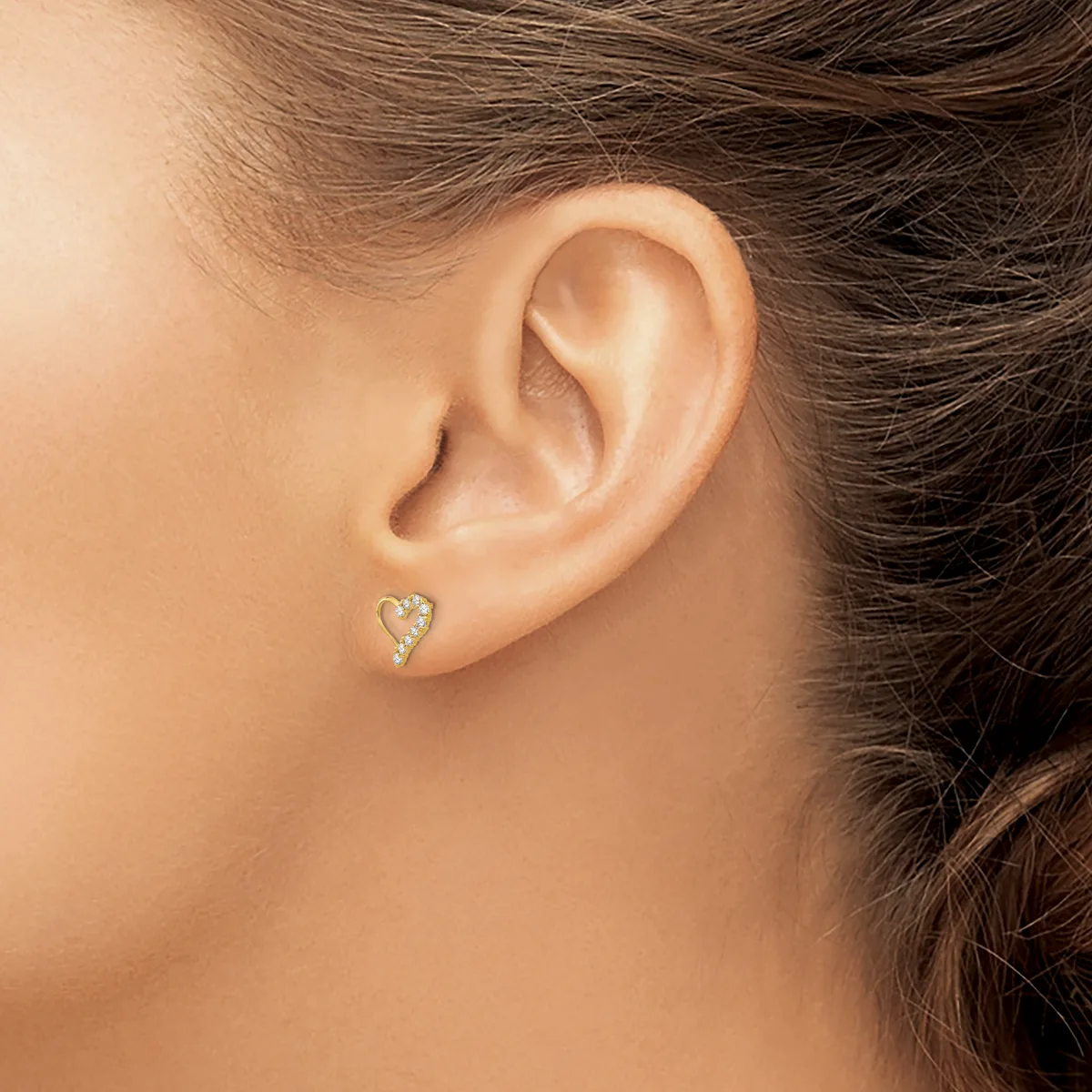 A person wearing a small heart-shaped stud earring with a textured surface on their earlobe.
