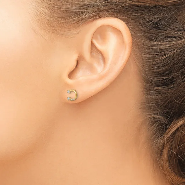 A person wearing a small curved crescent-shaped earring with diamond accents in the earlobe, shown from the side profile.