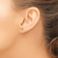 A person wearing a small square stud earring with a light green stone in a decorative setting, shown from the side view of their ear.