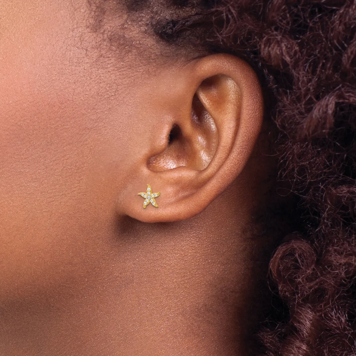 A small gold star-shaped stud earring in a pierced earlobe, shown in profile view against skin tone.