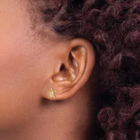 A person with dark curly hair wears a small gold turtle-shaped earring with a gemstone on their earlobe.