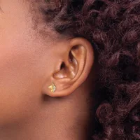 A person with dark curly hair wearing a small gold leaf-shaped earring with a textured surface in their pierced earlobe.