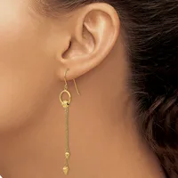 A woman wearing gold dangle earrings with small spherical beads on thin chains, shown from the side profile near her ear.